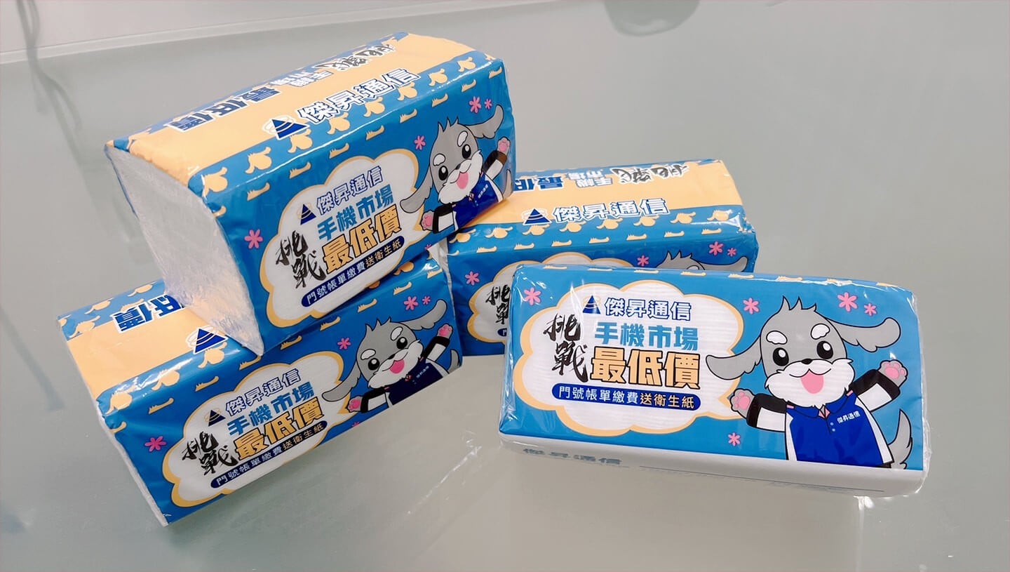 四包疊放在一起的傑昇通信促銷用抽取式衛生紙。包裝為藍黃配色，印有穿著制服的狗狗傑納瑞吉祥物，以及『手機市場最低價』、『門號帳單繳費送衛生紙』等宣傳字樣。