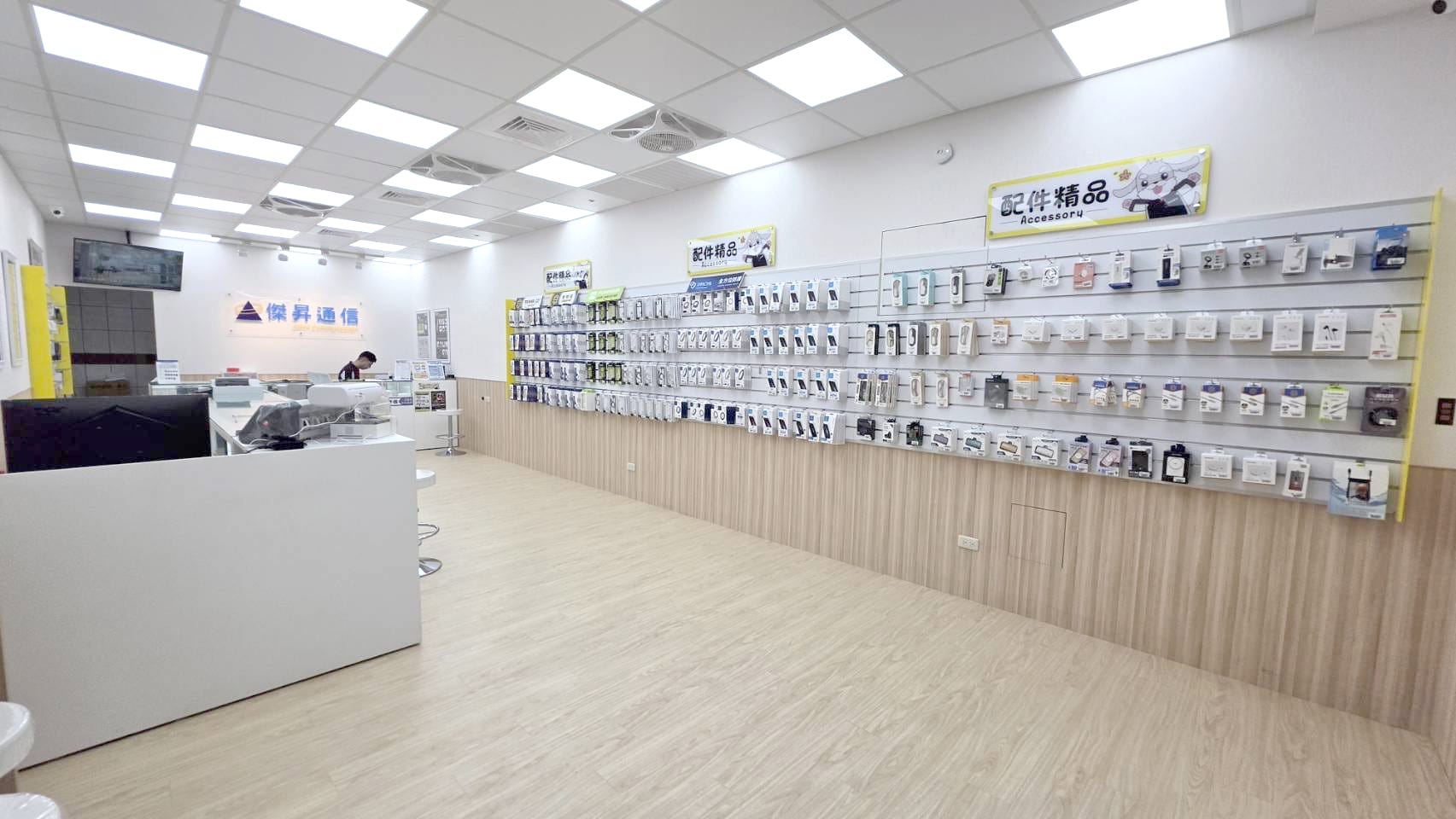 傑昇通信台中南屯黎明店內部實景。明亮寬敞的空間採用溫潤木質地板與白色系櫃台，牆面設有豐富的配件精品展示區，提供顧客舒適且專業的購機與挑選配件環境。