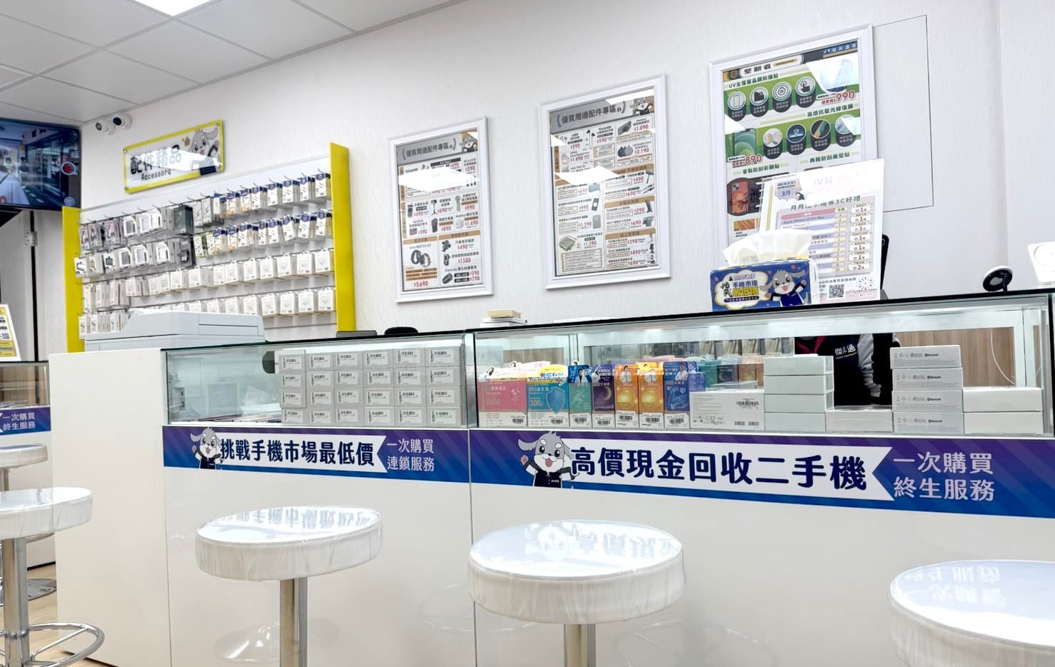 傑昇通信門市櫃檯與客座高腳椅，展示「挑戰手機市場最低價」與「高價現金回收二手機」服務標語。